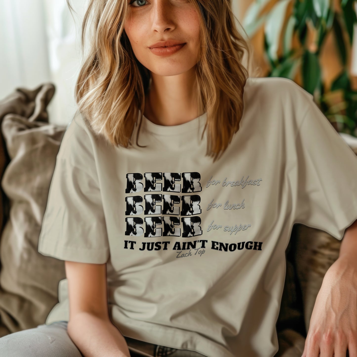 The front of the shirt displays the word "BEER" three times, each with a unique cow-print pattern, followed by the phrases "for breakfast," "for lunch," and "for supper" in a playful, cursive font. Below these, the shirt proudly declares, "IT JUST AIN'T ENOUGH,"