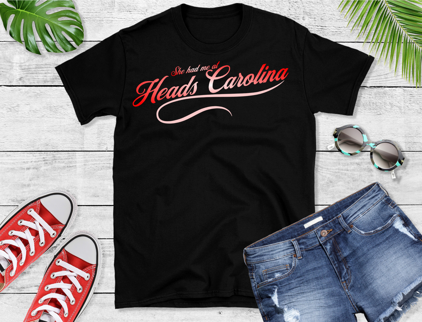 This stylish tee features a captivating design with the phrase "She had me at Heads Carolina" elegantly scripted in a gradient of red and pink hues. The text is beautifully arranged with "Heads Carolina" prominently displayed in a bold, cursive font,