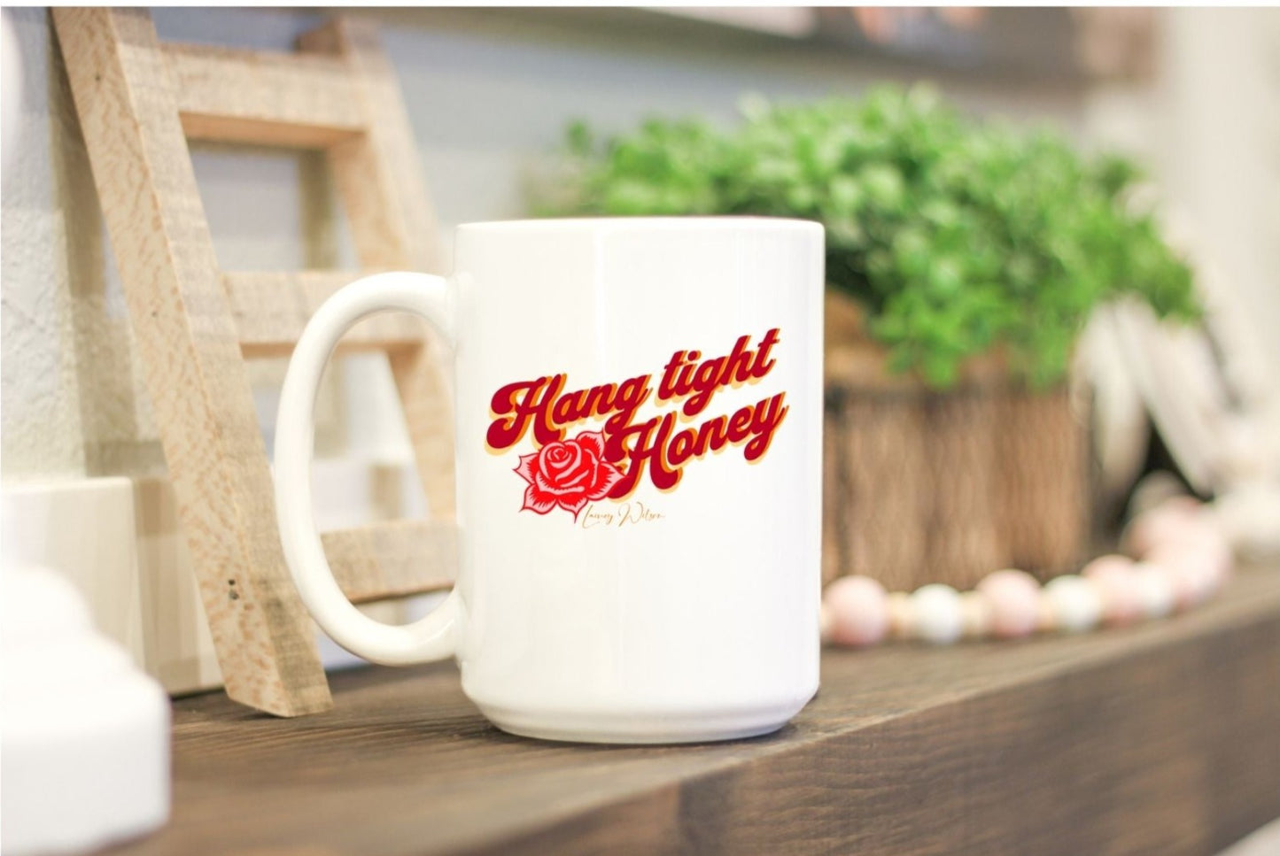 White coffee mug on the kitchen bench with the wording "hang tight honey" written in red, orange and yellow lettering