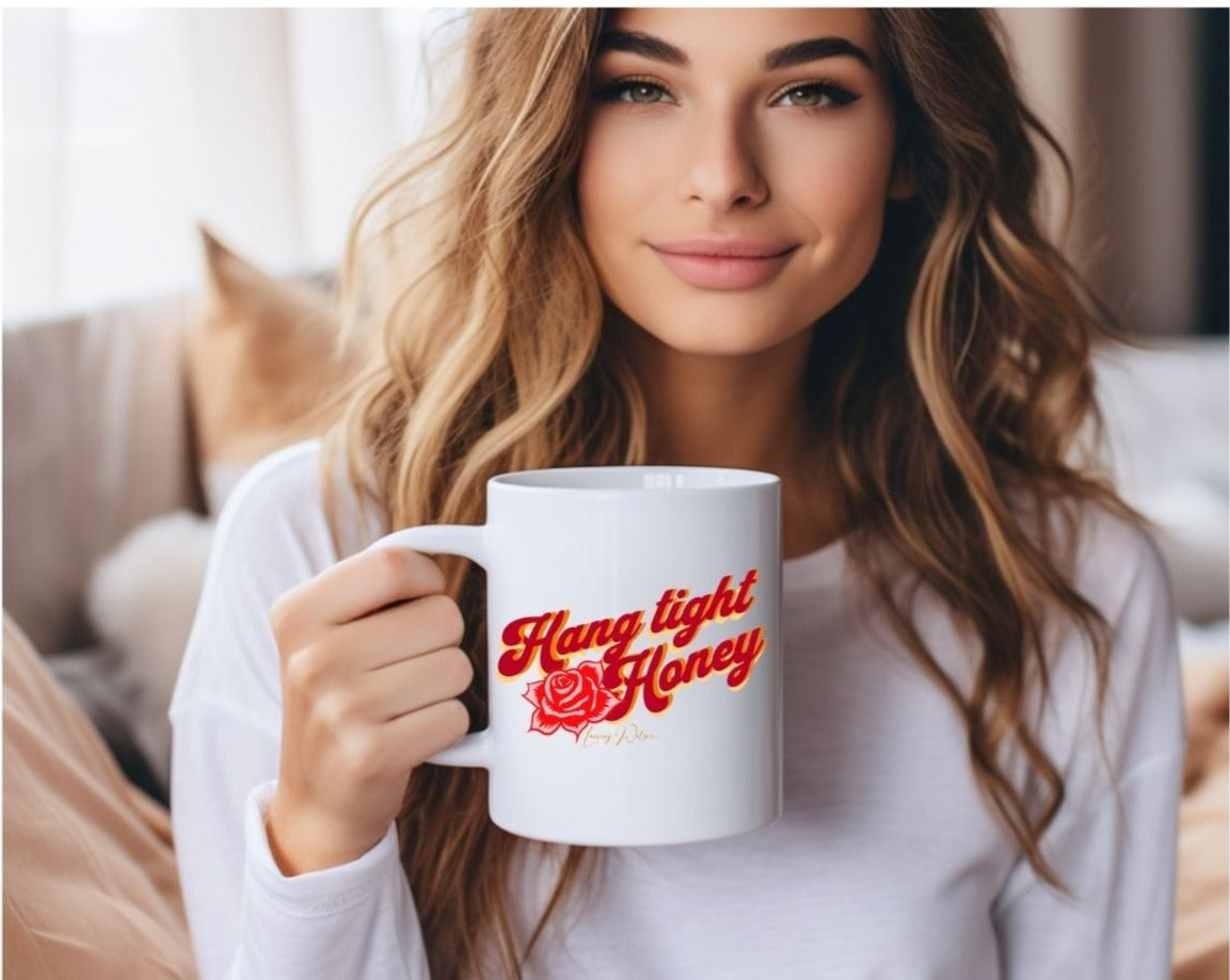 Lady sitting on a sofa holding a white mug with "Hang tight honey" written on it in red, orange and yellow lettering