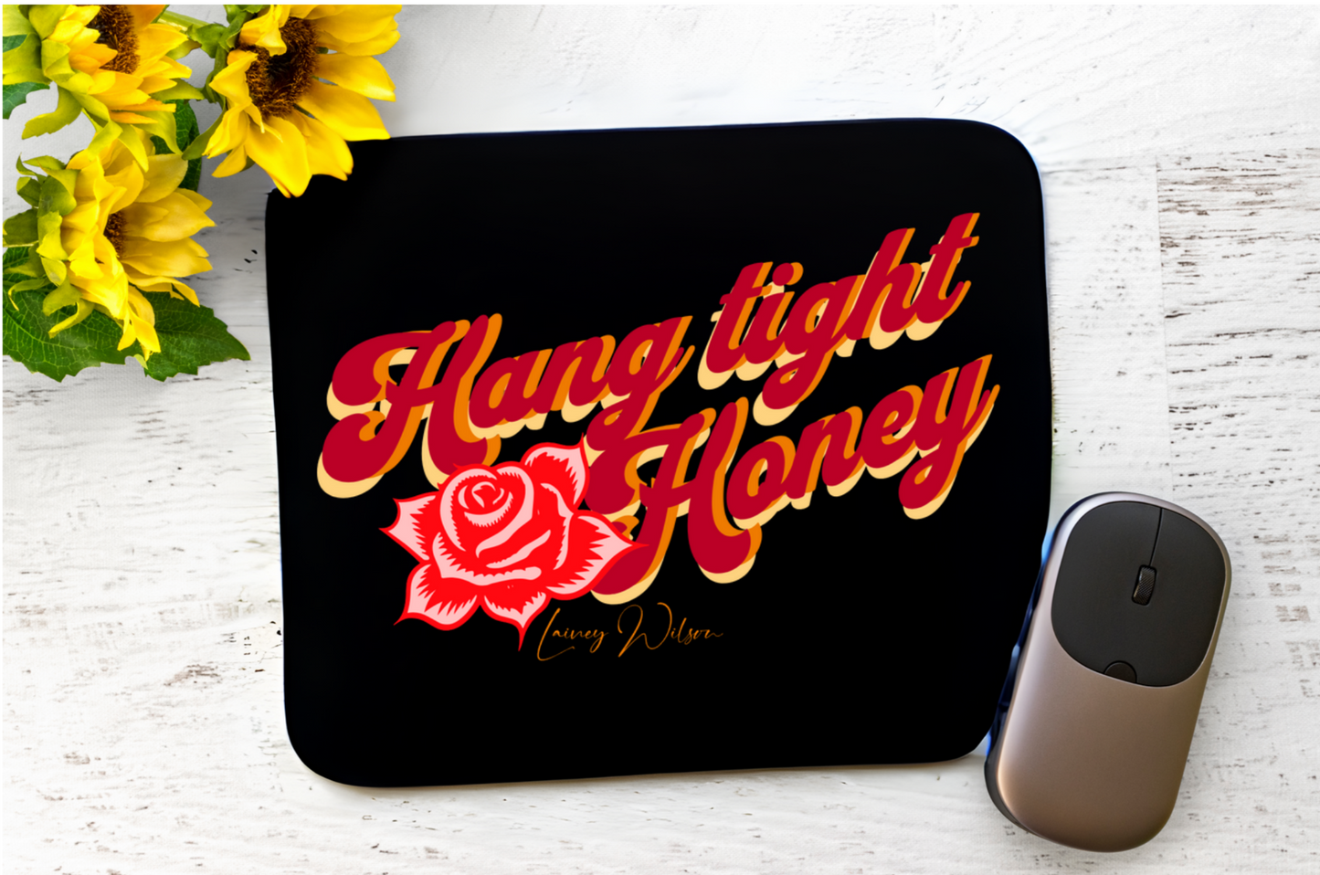 Black mouse paid with "hang tight honey" in red, orange and yellow test and Lainey Wilson written below. Image of a rose under the Hang
