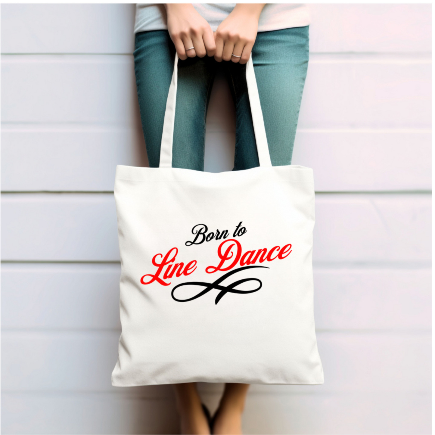 Lady holding the canvas tote bag with the black ornament under it.text "Born to" and red text "Line Dance" on it with a black