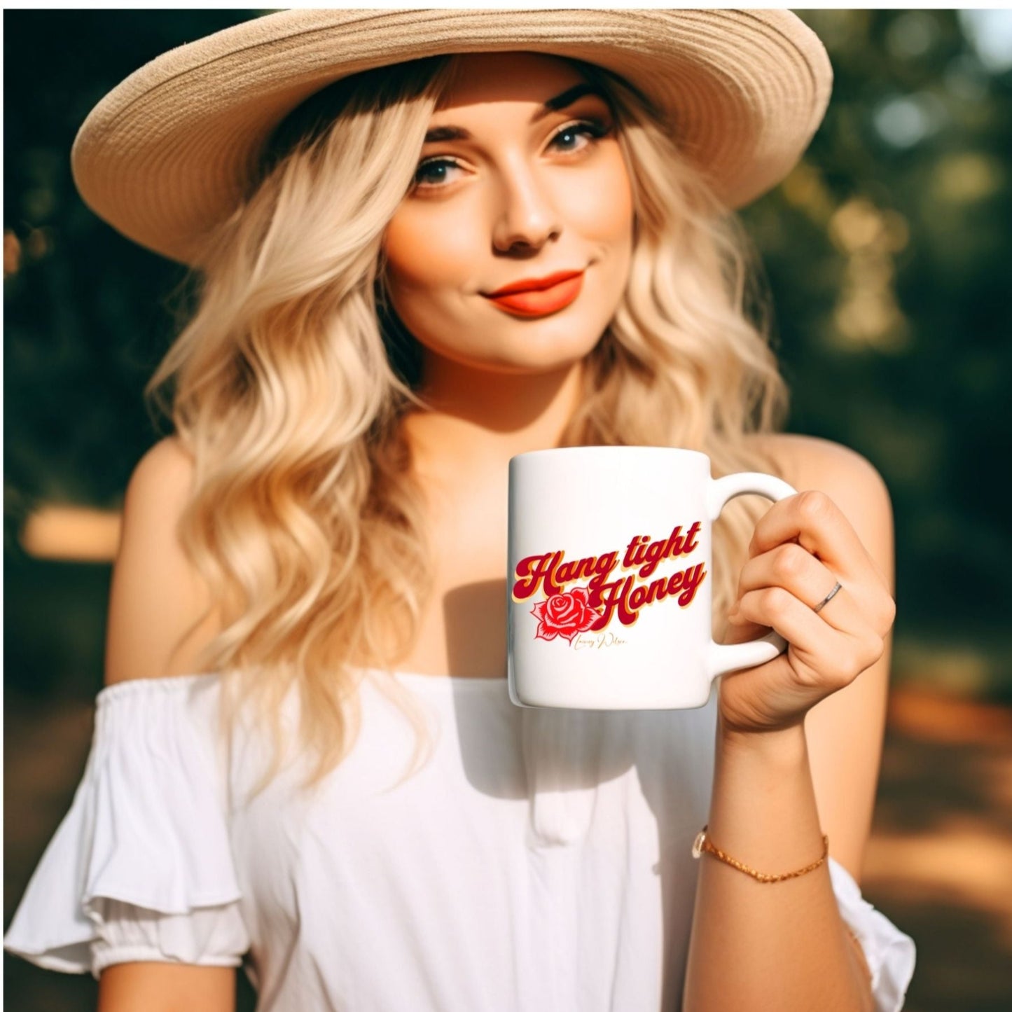 Lady sitting outside holding a white coffee mug with the wording "Hang tight honey" written on it in red, orange and yellow letttering