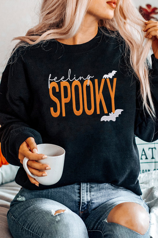 Person wearing a black sweatshirt with 'feeling Spooky' text, holding a white mug.