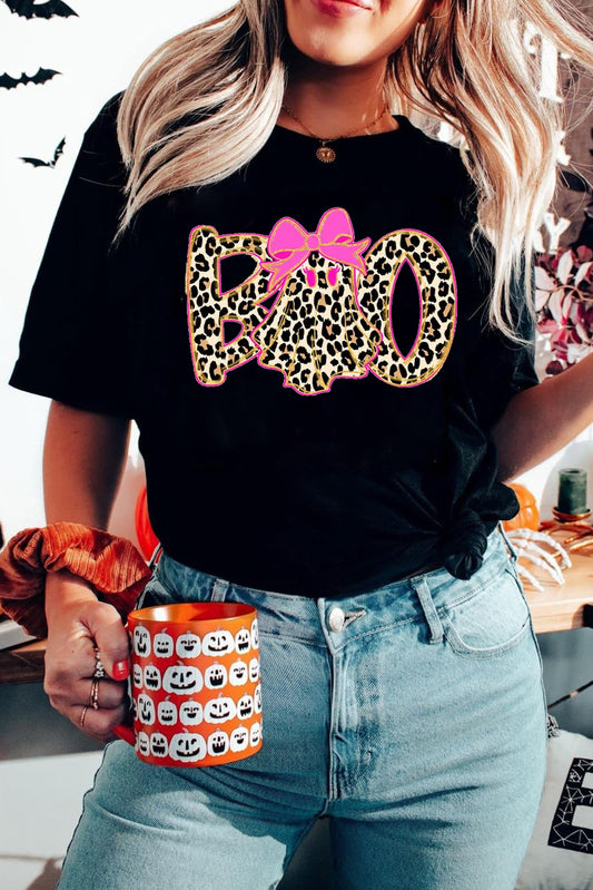 Person wearing a black t-shirt with leopard print and pink bow design, holding a Halloween-themed mug.