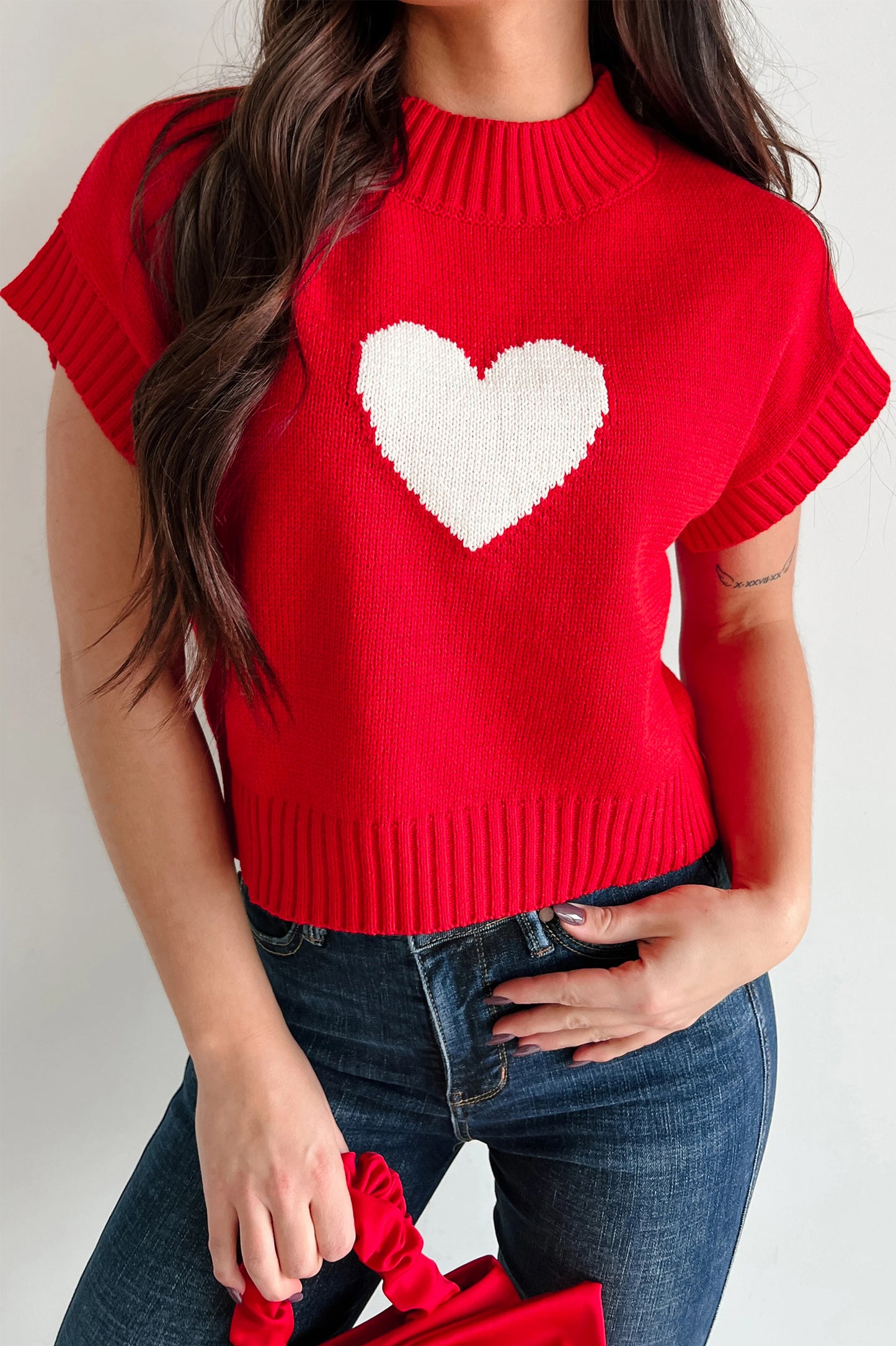 Red sweater with a white heart design worn by a person on a plain background