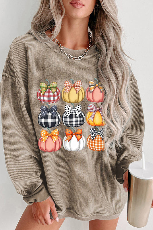 Person wearing a beige sweatshirt with colorful pumpkin designs, holding a cup.