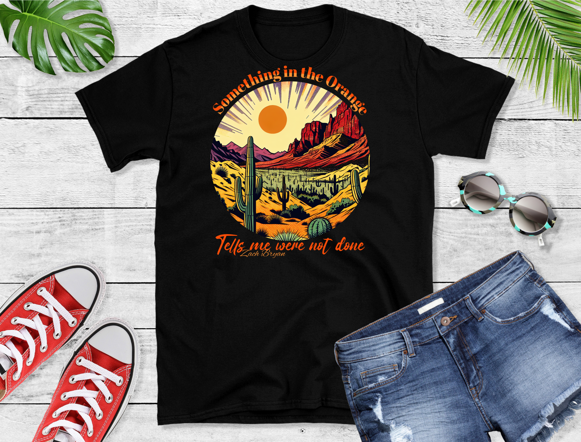  The design features a stunning desert landscape at sunset, complete with cacti and mountains, all bathed in a warm orange glow. The lyrics “Something in the Orange” and “Tells me we’re not done” frame the scene