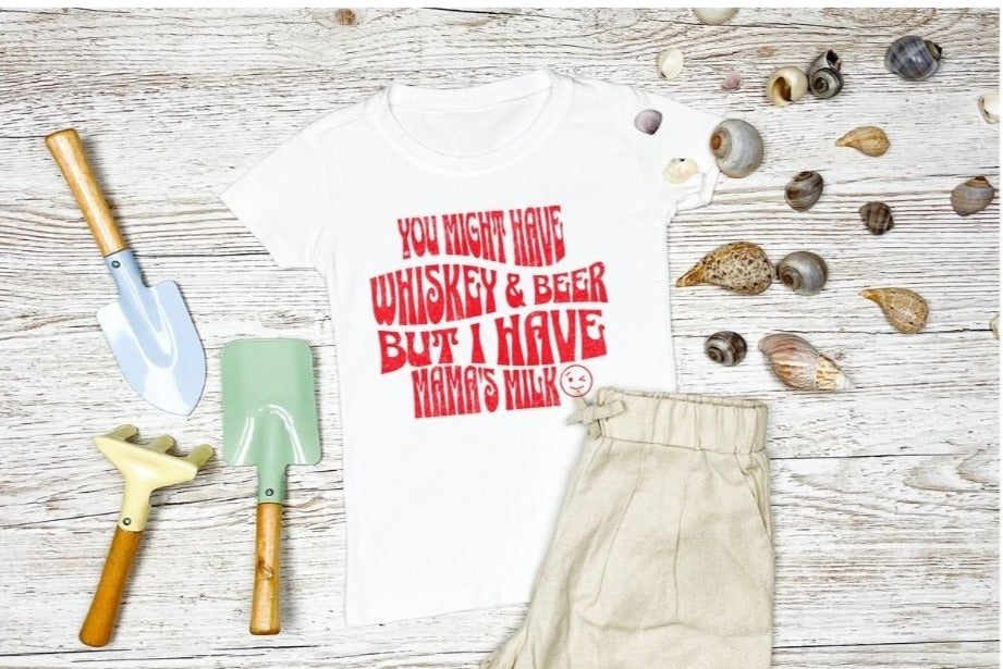 Kids T-Shirt pictured in a beach scene, with the red wording "you might have whiskey & beer but Ihave mama's milk 