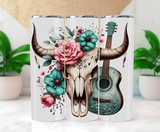 Features a majestic bull skull with prominent horns is adorned with vibrant flowers, including large pink roses, teal blooms, and an array of smaller pink and purple flowers, all set against a backdrop of lush green foliage. Leaning against the skull is a turquoise acoustic guitar with intricate designs