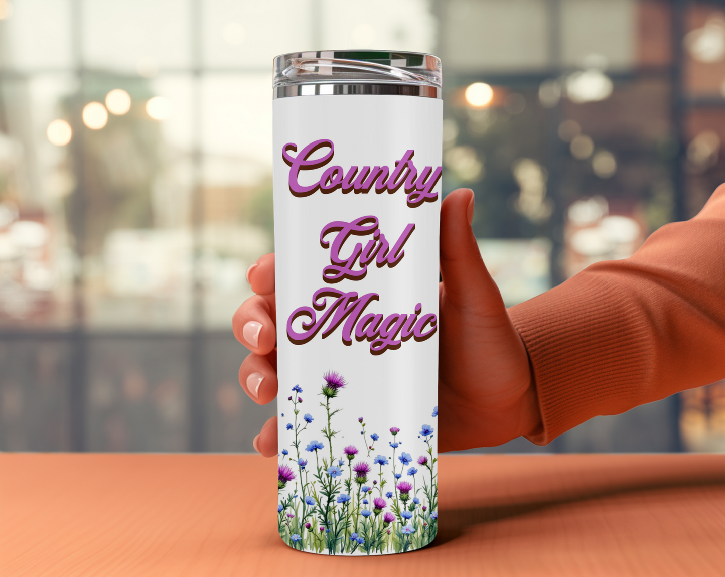 Features a vibrant display of wildflowers, with delicate blue blossoms and striking purple thistles, set against a pristine white background. The phrase "Country Girl Magic" is prominently displayed