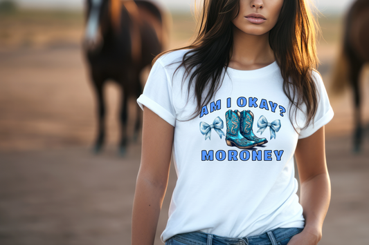 This eye-catching tee features a bold graphic of vibrant blue cowboy boots, intricately designed with swirling patterns that evoke a sense of classic country charm. Flanking the boots are two matching blue bows, adding a touch of feminine flair to the rugged design. Above the boots, the question “AM I OKAY?” is emblazoned in large, attention-grabbing letters, while Moroney’s name anchors the image below in confident typography.
