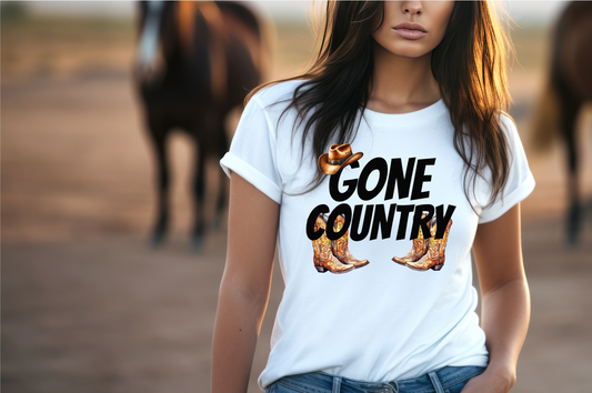 The front of the shirt showcases the phrase "GONE COUNTRY" in large, black letters, making a statement that resonates with every country music lover. Above the text, a classic brown cowboy hat adds a touch of rustic charm, while below, a pair of intricately designed cowboy boots.