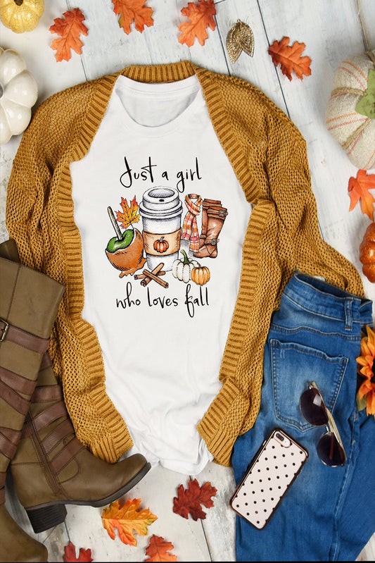 White t-shirt with autumn-themed design, mustard sweater, blue jeans, brown boots, and phone case on a white surface with fall decorations.