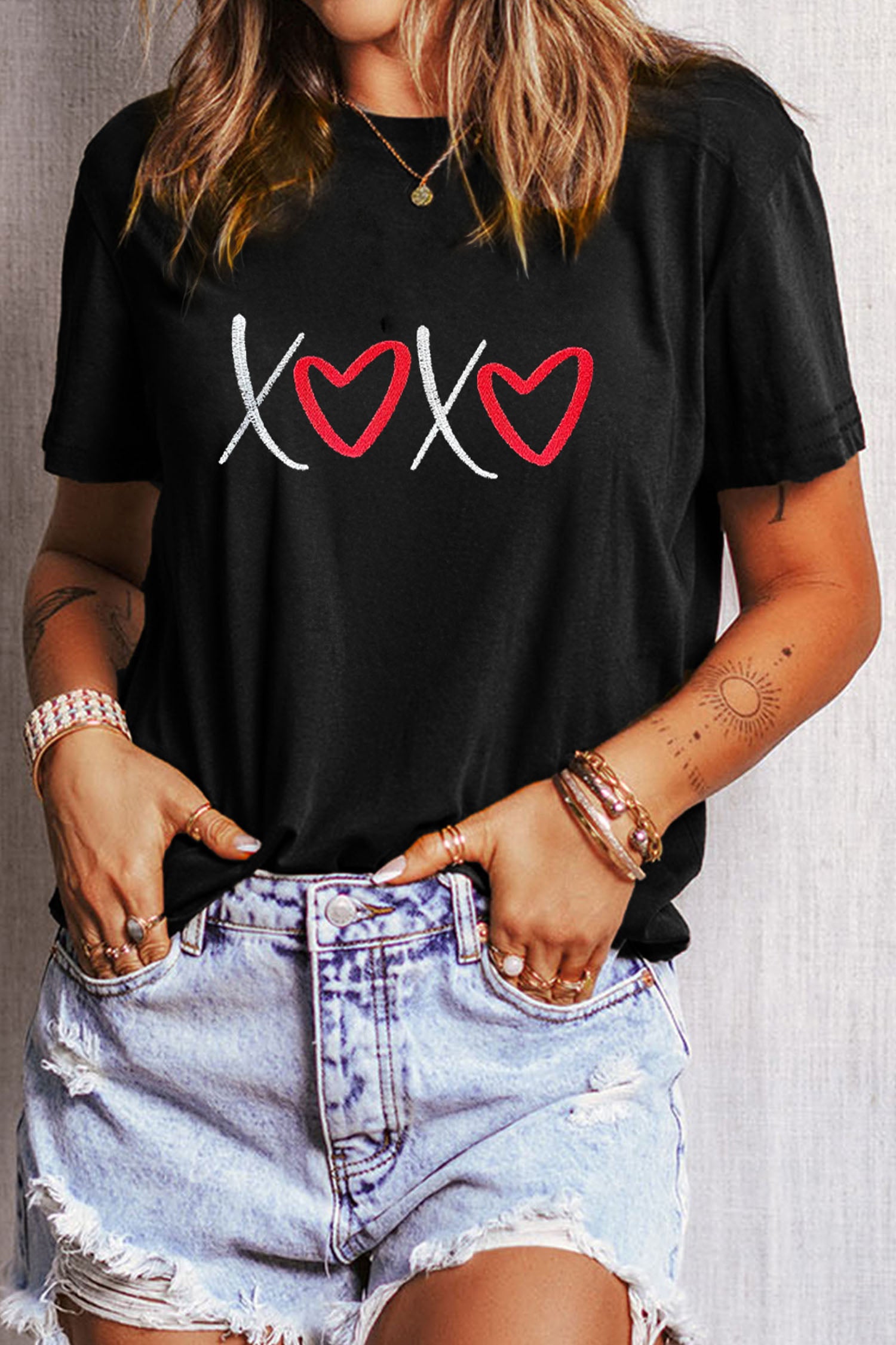 Person wearing a black t-shirt with heart designs and denim shorts.