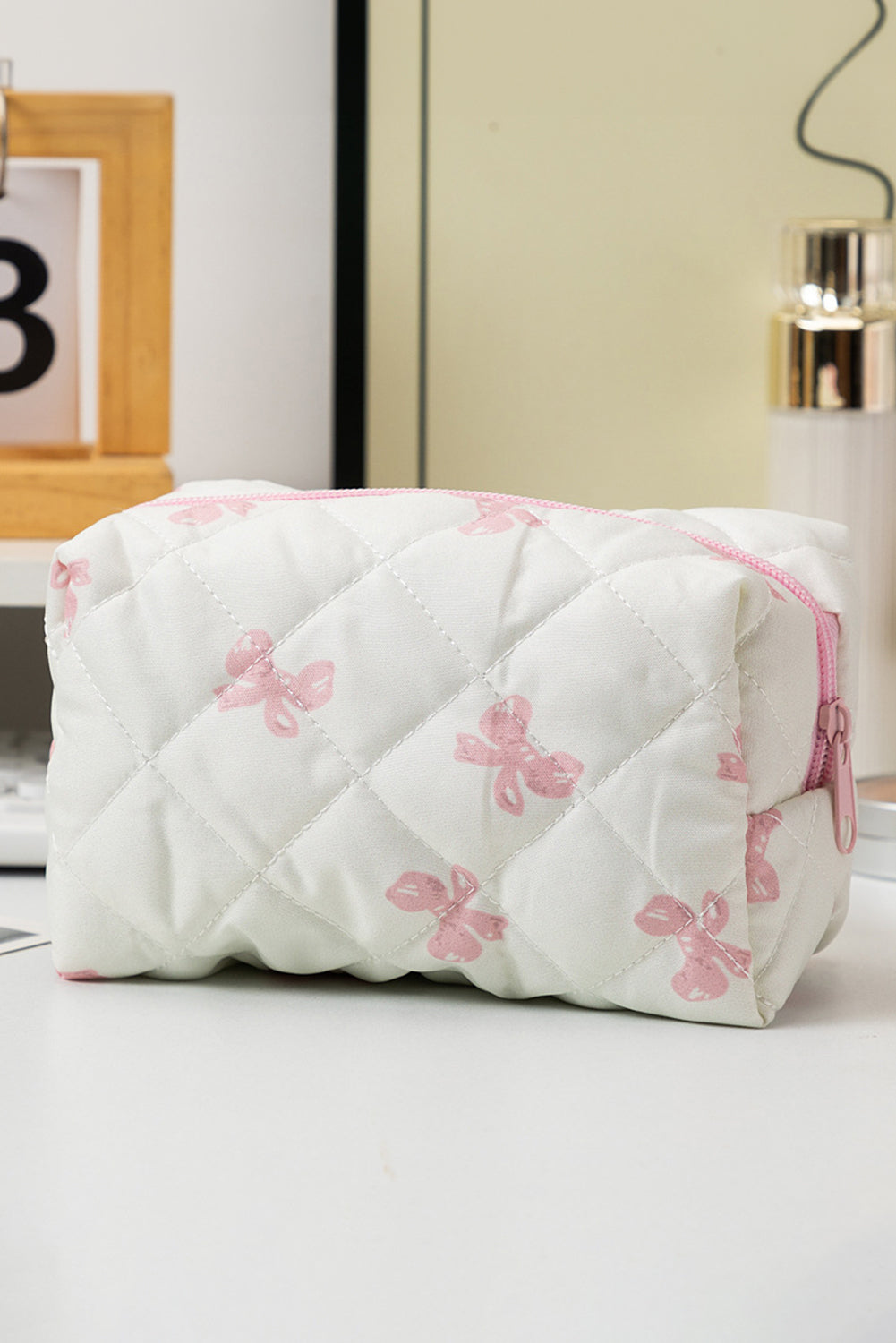 White quilted cosmetic bag with pink floral patterns and a zipper on a light surface.